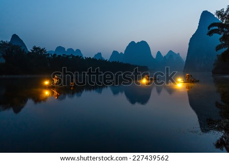 XINGPING, CHINA - OCTOBER 21, 2014: Cormorant fishermans stands on the ancient bamboo boat with a lighted lamps in their hands - The Li River, Xingping, China