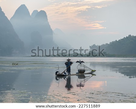 XINGPING, CHINA - OCTOBER 21, 2014: Cormorant fisherman stands on the ancient bamboo boat - The Li River, Xingping, China