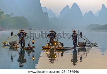 XINGPING, CHINA - OCTOBER 23, 2014: Cormorant fisherman on the ancient bamboo boat with a lighted lamps and cormorants in the sunrise - The Li River, Xingping, China