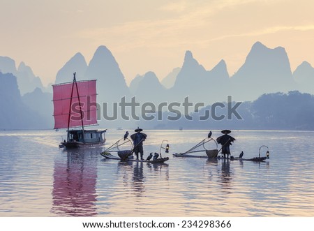 XINGPING, CHINA - OCTOBER 23, 2014: Fishermans stands on traditional bamboo boats at sunrise (boat with a red sail in the background) - The Li River, Xingping, China