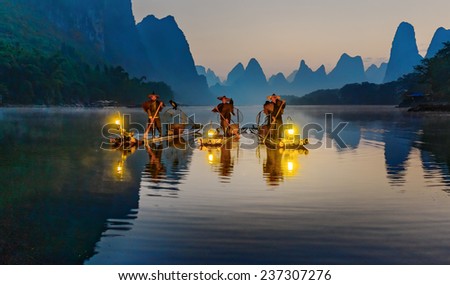 XINGPING, CHINA - OCTOBER 22, 2014: Cormorant fishermans stands on the ancient bamboo boat with a lighted lamps and cormorants in the sunrise - The Li River, Xingping, China