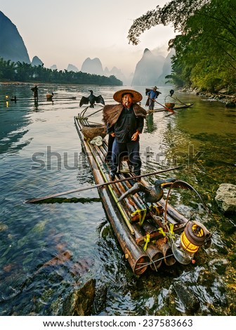 XINGPING, CHINA - OCTOBER 21, 2014: Cormorant fisherman on the ancient bamboo boat with a lighted lamps and cormorants in the sunrise - The Li River, Xingping, China