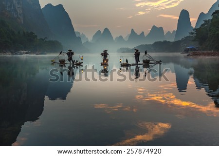 XINGPING, CHINA - OCTOBER 22, 2014: Cormorant fisherman stands on the ancient bamboo boat with a lighted lamps and cormorants in the sunrise - The Li River, Xingping, China