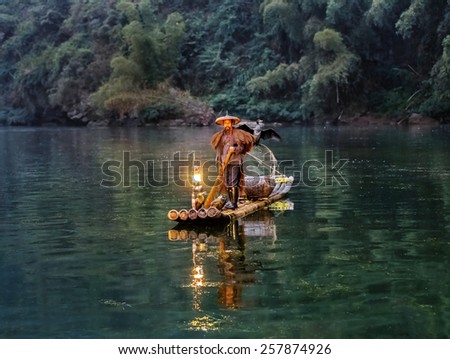 XINGPING, CHINA - OCTOBER 21, 2014: Cormorant fisherman stands on the ancient bamboo boat with lamp in the sunrise - The Li River, Xingping, China