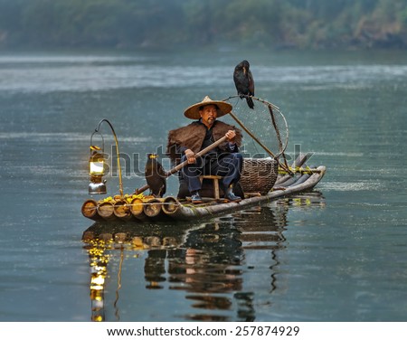 XINGPING, CHINA - OCTOBER 21, 2014: Cormorant fisherman sits on the ancient bamboo boat with lamp in the sunrise - The Li River, Xingping, China