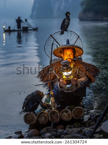 XINGPING, CHINA - OCTOBER 24, 2014: Cormorant fisherman sits in his ancient bamboo boat with lamp in hand after a successful fishing - The Li River, Xingping, China