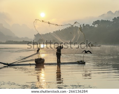 Cormorant fisherman throws a net with ancient bamboo boats at sunrise - Xingping, China