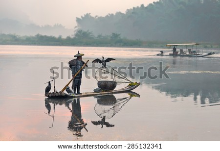 XINGPING, CHINA - OCTOBER 24, 2014: Cormorant fishermen on ancient bamboo boats with lighted lamps and cormorants - The Li River, Xingping, China