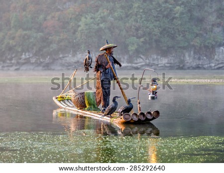XINGPING, CHINA - OCTOBER 22, 2014: Cormorant fishermen on ancient bamboo boats with lighted lamps and cormorants - The Li River, Xingping, China