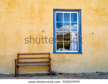 Old looking yellow wall with blue wooden window and a bench