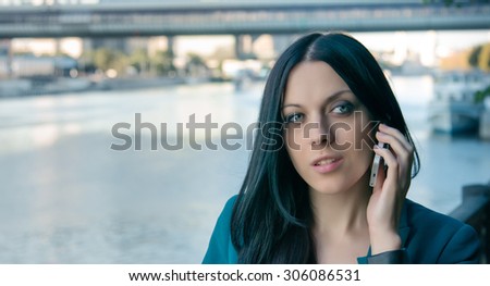 Business woman speaks on the phone near the river.
