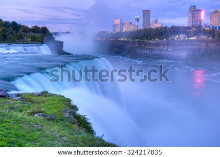 Flowing Niagara Falls from the American side with the skyline of the city of Niagara Falls in the background at dawn. The Niagara Falls is one of the largest and most famous waterfall in the world.