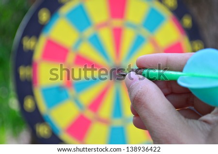 A hand holding a dart getting ready to aim at the dartboard