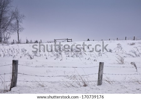 Scenic winter farm landscape with barbed wire fence in the foreground.  Hoarfrost clings to wire and trees.  Winter in Wisconsin