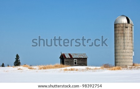 Old, abandoned farm homestead.  Silo and small farm house against bright blue winter sky.