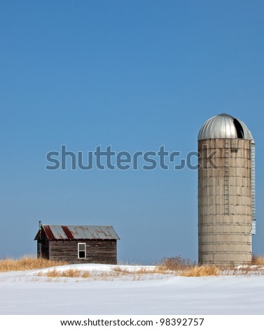Old, abandoned farm homestead.Silo and small farm house against bright blue winter sky.