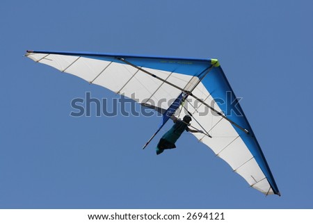 A man hang gliding overhead against a brilliant blue sky