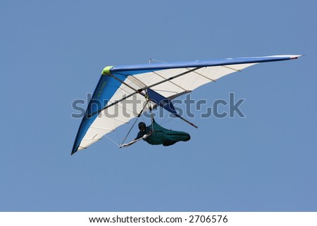 A man hang gliding overhead against a brilliant blue sky