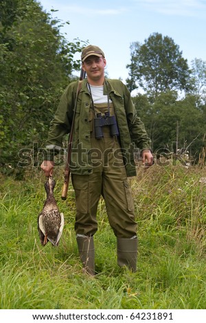 Hunter with duck in hand on a meadow.