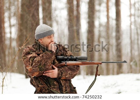 Smoking hunter with rifle at winter forest.