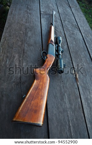 Sniper rifle with optical sight on wooden table.