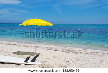 white surfboard and yellow beach umbrella on the sand