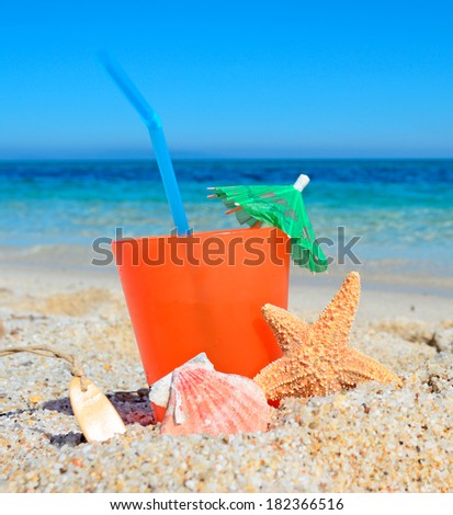 orange drink with shell and umbrella by a tropical beach