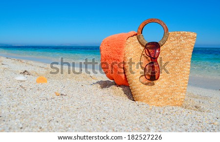 sunglasses, towel and straw bag by a tropical beach
