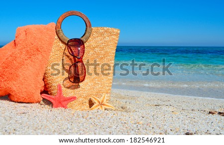straw bag with sunglasses and towel at the beach