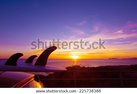 car with surfboard by the shore at sunset. Shot in Alghero, Capo Caccia in the background. Sardinia, Italy