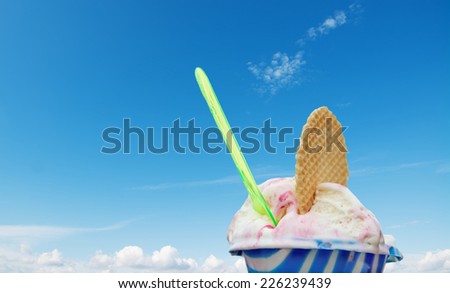 cup of cherry ice cream with wafer and spoon under a blue sky with clouds