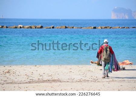 seller walking on the beach in Alghero shore. Capo Caccia on the background on a sunny day.