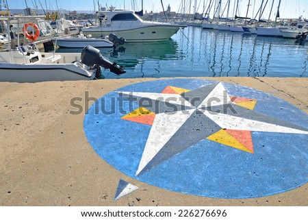 wind rose painted on Alghero harbor.Boats in the background on a sunny day