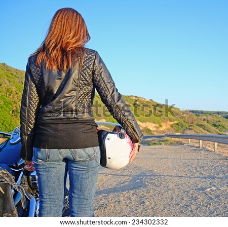 biker girl and motorcycle on the edge of the road at sunset