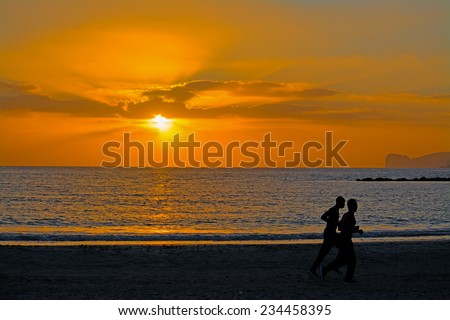 two black men running on the shore at sunset.