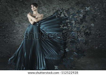 Young fairy woman in long dress made from butterflies flying out under wind