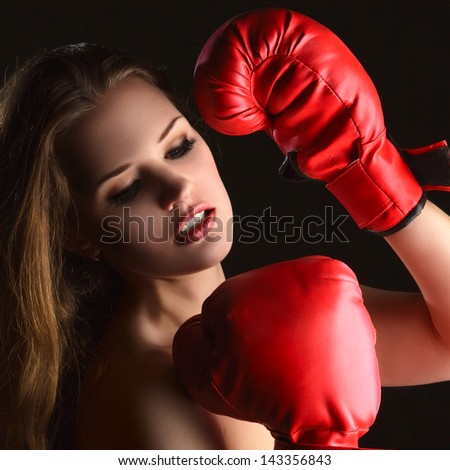 Young blonde woman with boxing gloves against dark background