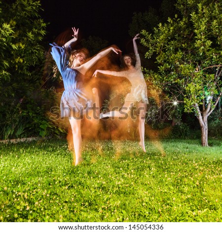 Two young woman dancing at night garden. Long time exposure