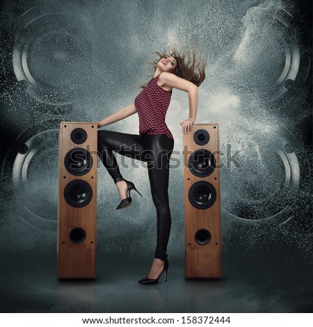 Abstract concept of powerful audio speakers blast out a cloud of dust against dark background and dancing woman posing in front of them