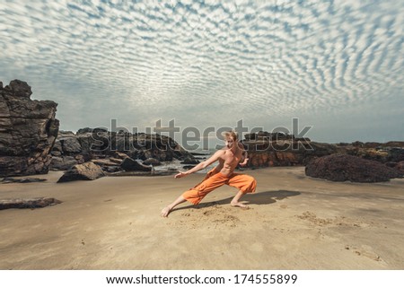 Young man doing martial arts training with sunset sea view at background