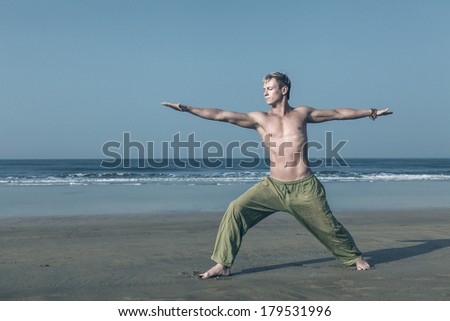 Young man doing yoga and meditating in warrior pose at sea beach