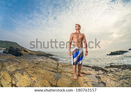Athletic handsome man in swimming shorts posing in front of tropical sea