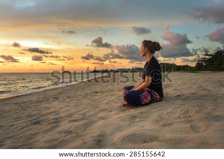 Woman sitting on beach sand and relaxing at sunset time