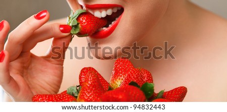 Young woman eating red ripe strawberry close-up studio shot