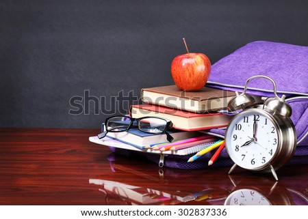 Books, apple, backpack, alarm clock and pencils on wood desk table and black board. Back to school concept
