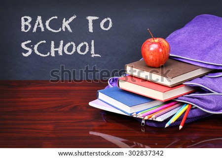 Books, apple, backpack and pencils on wood desk table. Text back to school on black board concept