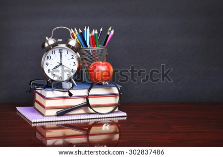 Books, apple, alarm clock and pencils on wood desk table and black board. Back to school concept
