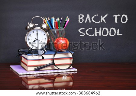 Books, apple, alarm clock and pencils on wood desk table. Text back to school on black board concept