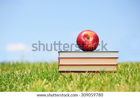 Fresh apple and books on green grass. Back to school
