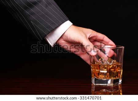 rich and success business man holding in hand glass of alcohol scotch whiskey with ice cube on wooden table and black background